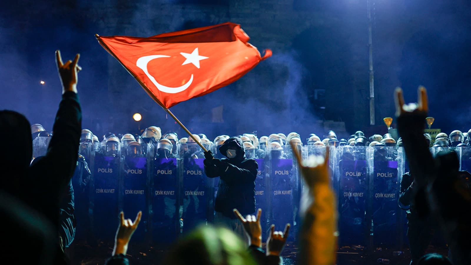 A masked protester waves a large Turkish flag in front of a line of riot police during a night-time demonstration in Istanbul.